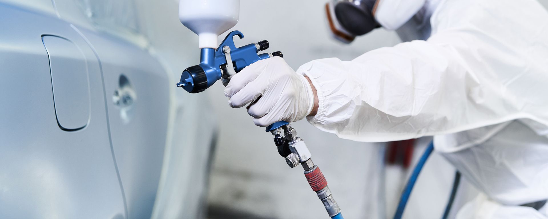 Ein Arbeiter in Schutzkleidung, einschließlich Atemschutzmaske, lackiert mit einer Spritzpistole ein Auto in einer Werkstatt